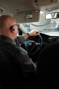 Bald taxi driver with earpiece driving a Volkswagen while wearing a watch.